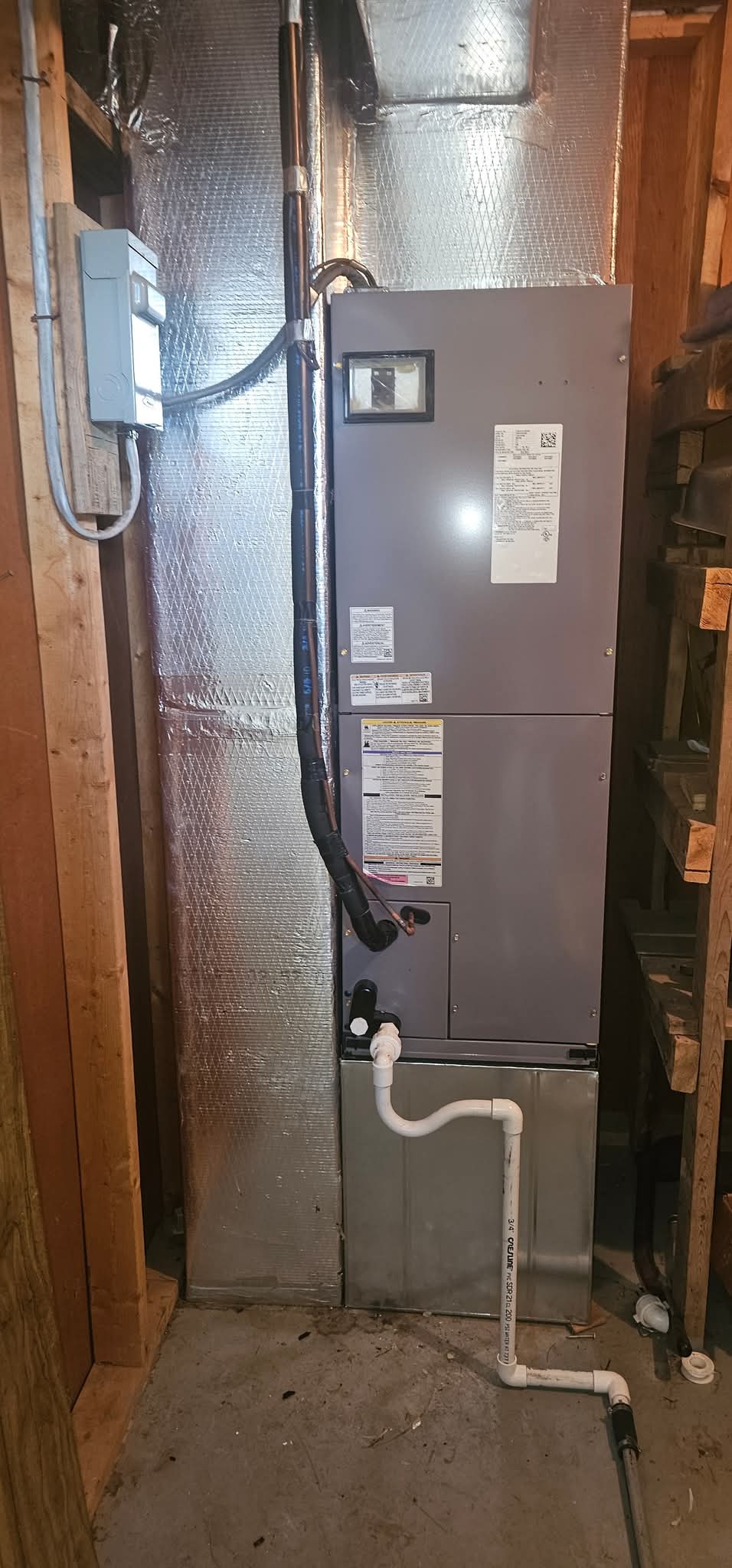 A central HVAC unit with visible ductwork and PVC drainage pipes is installed in a wooden utility room with shelves on the right.