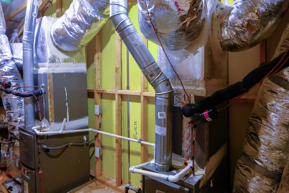 Two HVAC units with insulated ducts and pipes installed in an unfinished room with exposed wall framing and yellow insulation.